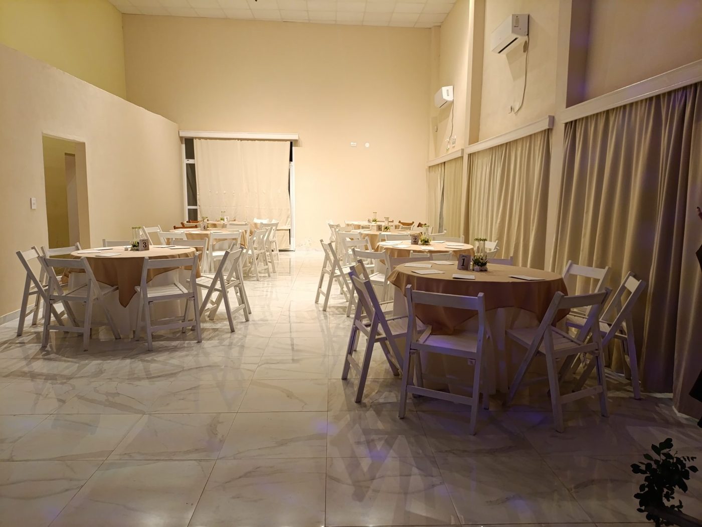 Salón armado con mesas redondas y sillas blancas