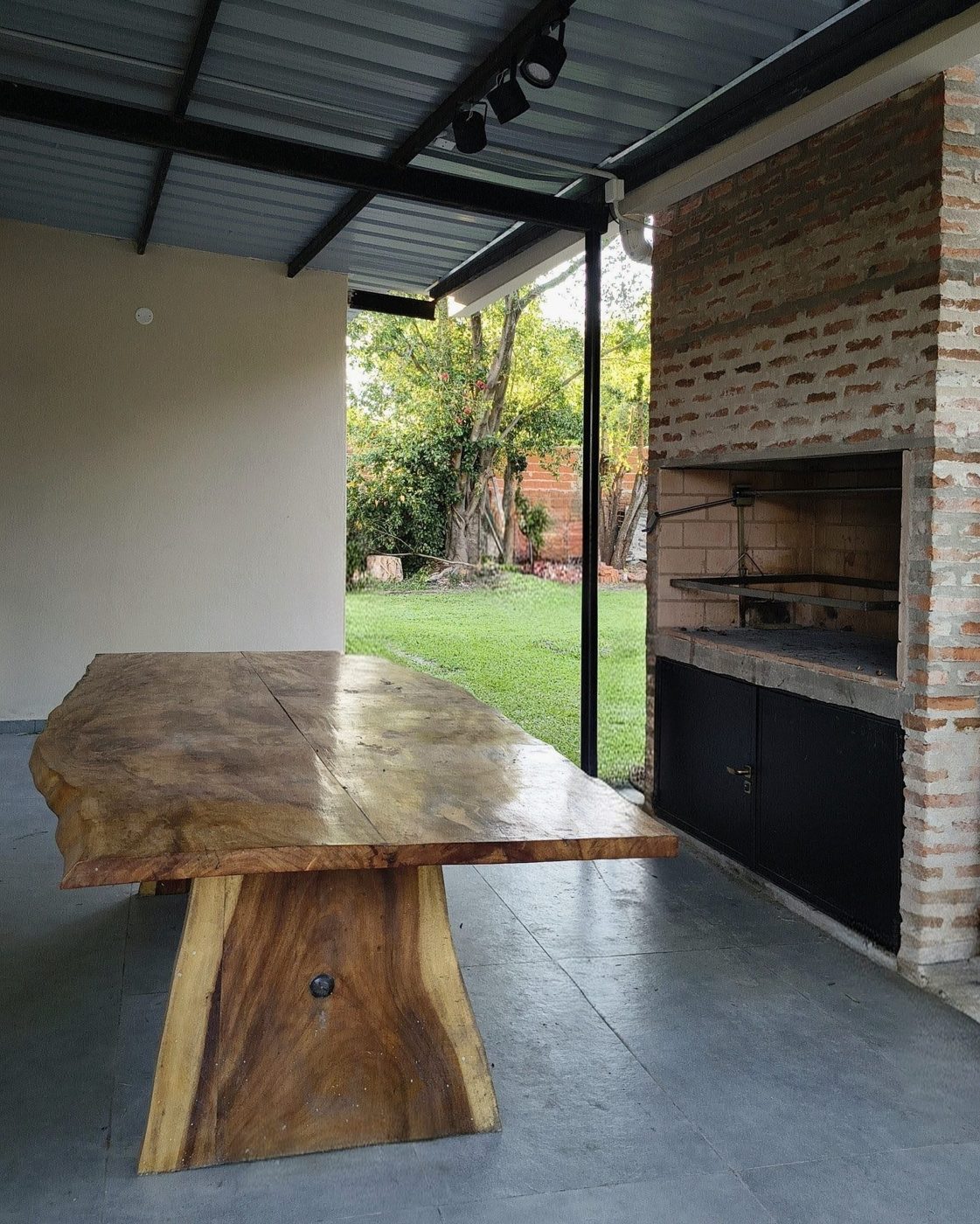 Parrilla de ladrillo y mesa de madera en la galería