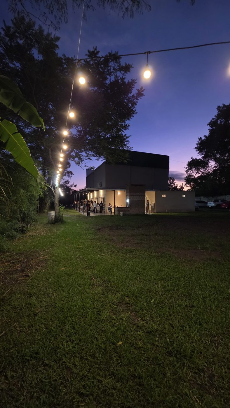 El parque de Raíces al anochecer, con guirnaldas de luces y el salón iluminado al fondo